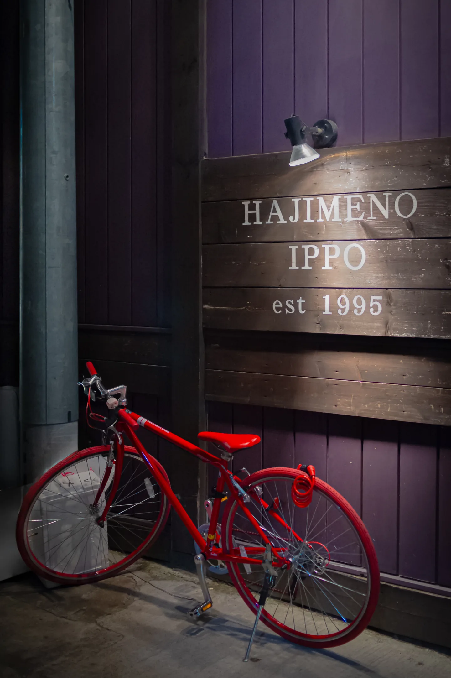 A red bicycle beneath the illuminated Hajime no Ippo sign at night in Japan