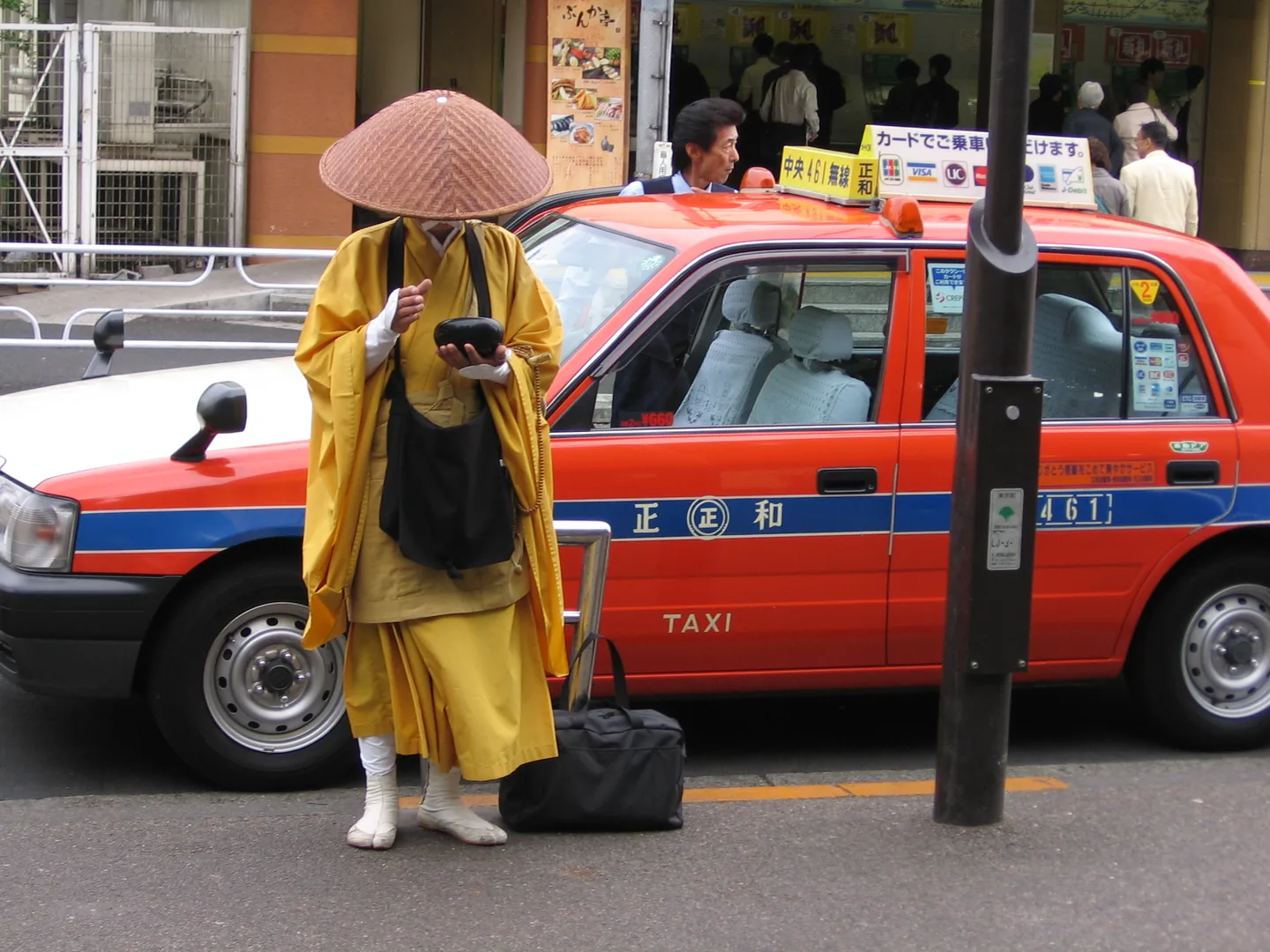 A monk walking along a Tokyo street beside a taxi