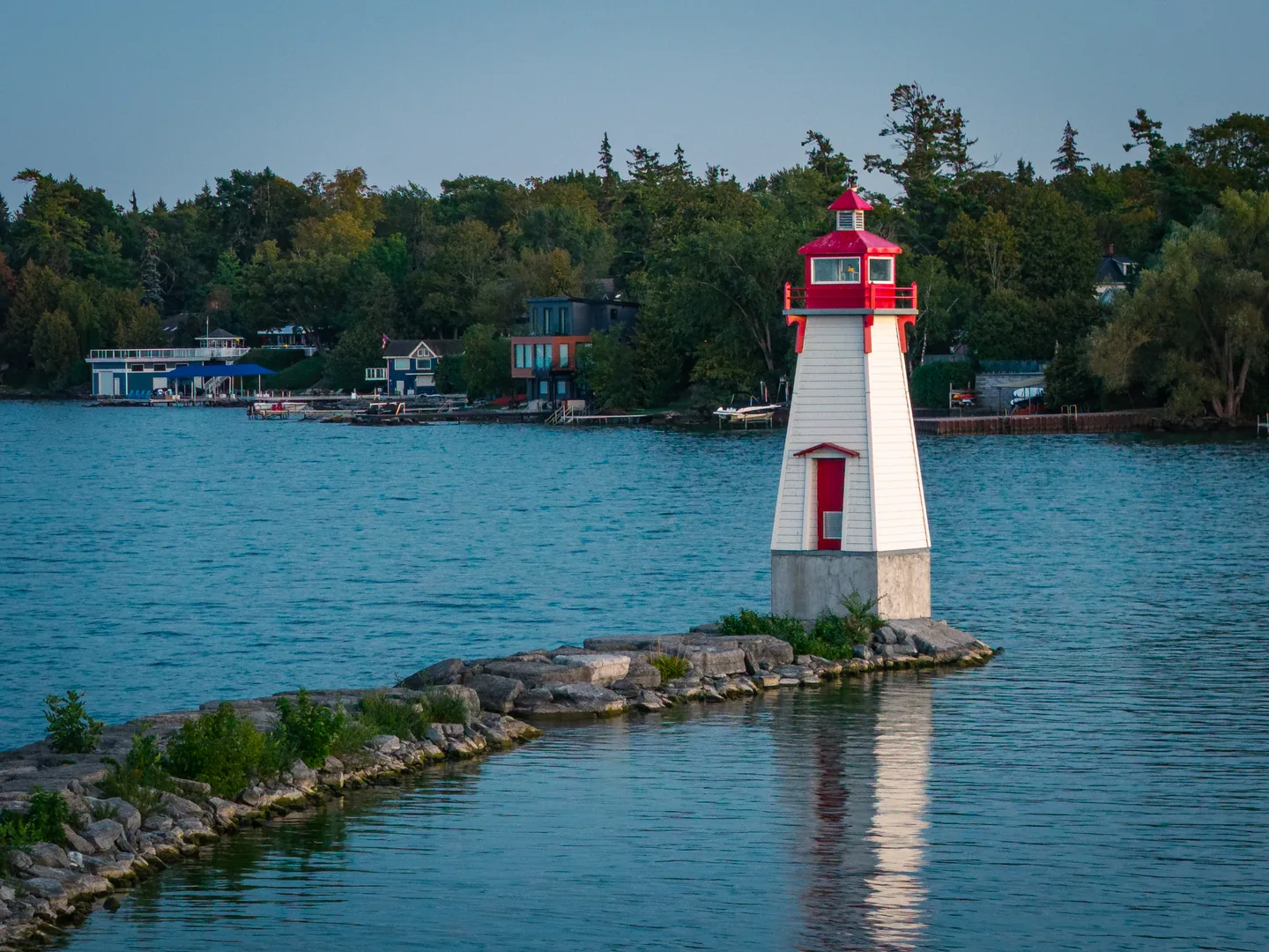A red-and-white lighthouse at Jackson's Point, reached by a diagonal stone breakwater across blue water